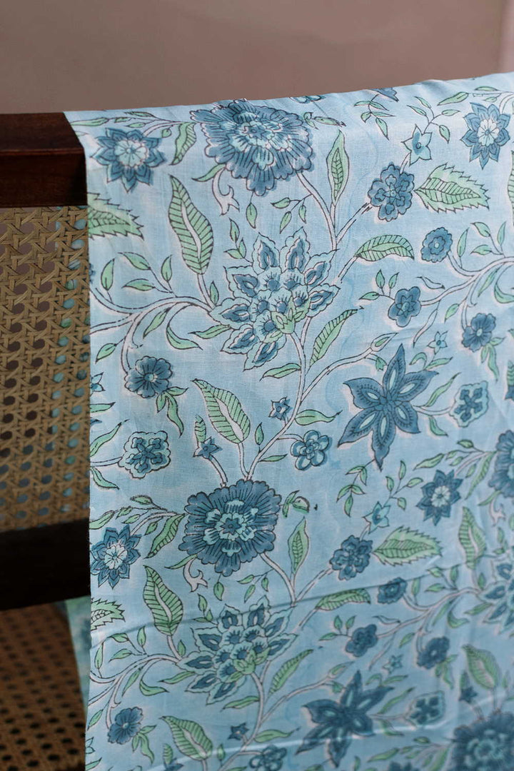 Floral patterned fabric with blue flowers and green leaves on a light blue background.